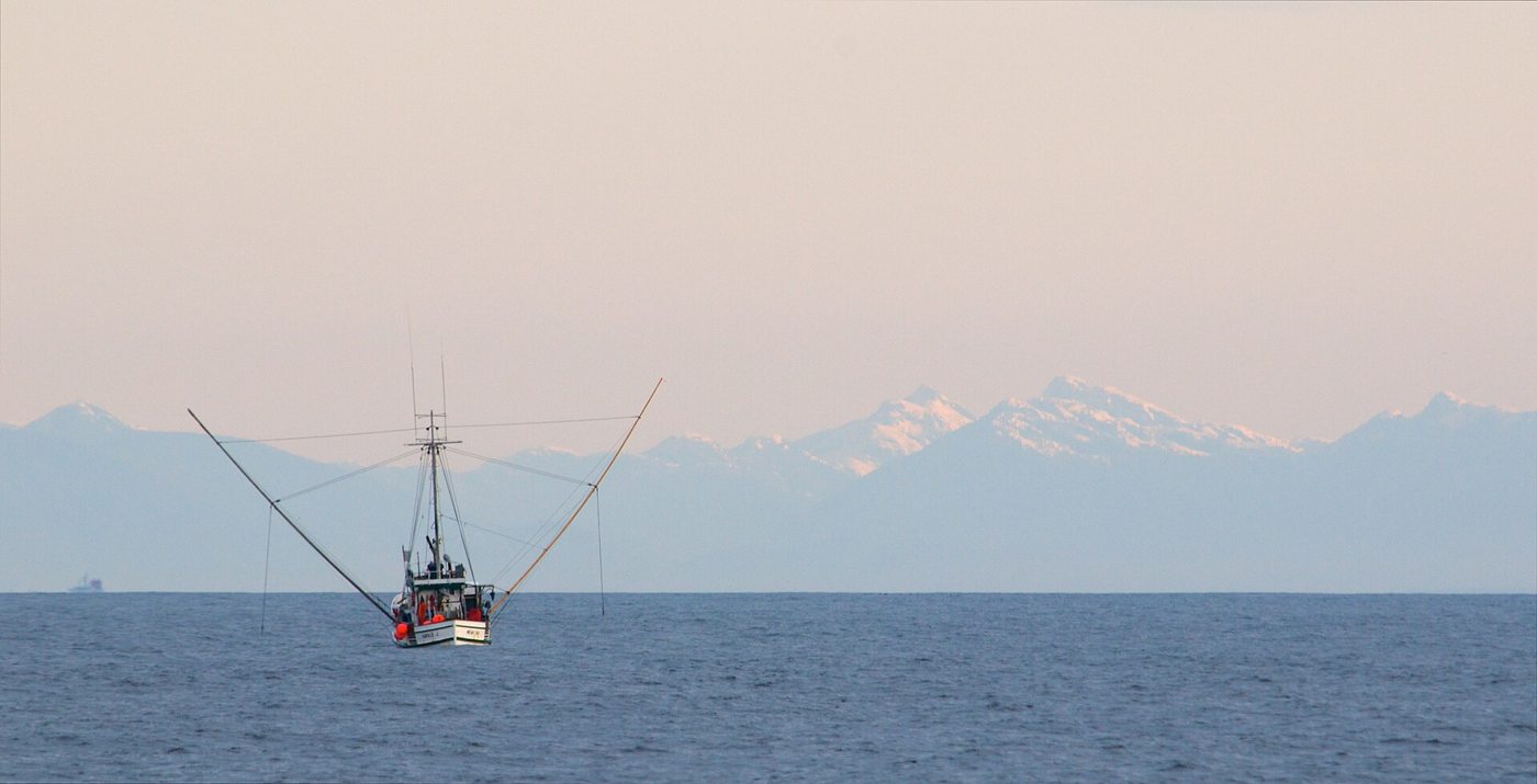The snow capped mountains of Vancouver Island form a backdrop for a fishing boat plying the calm waters of the Strait of
